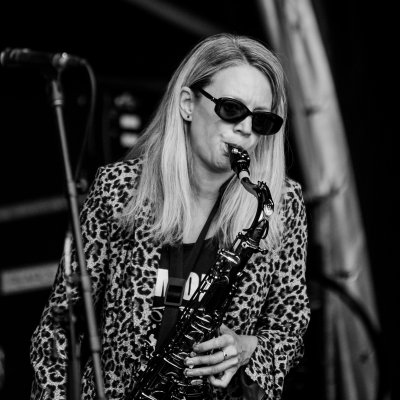 Liz Mitchell playing saxophone at outdoor festival, black and white