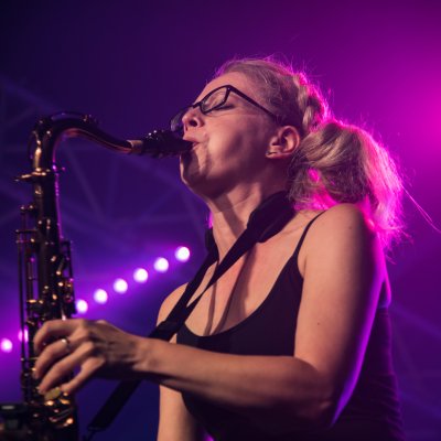 Liz Mitchell playing tenor saxophone with purple stage lighting
